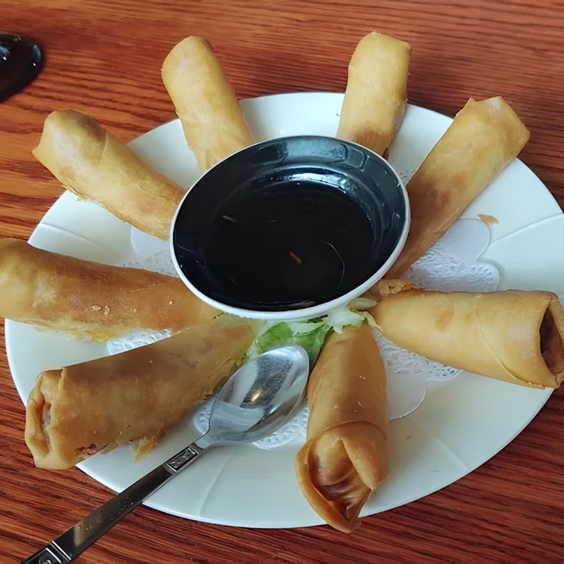 A plate of golden-brown Tong Thai spring rolls arranged around a dark dipping sauce bowl.