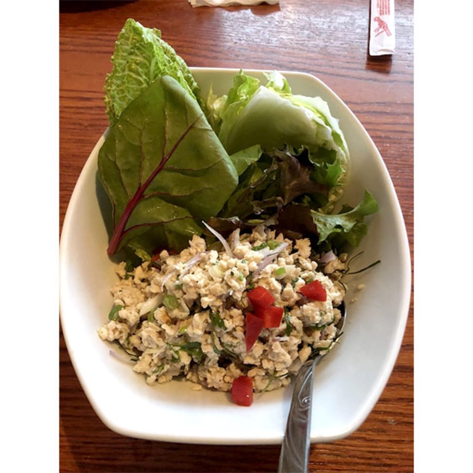 A white bowl of Thai larb with minced meat, red peppers, and lettuce wraps on a wooden table.