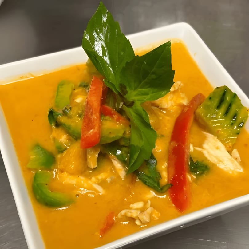 Tong Thai red curry with chicken, red bell peppers, avocado, and basil in a white bowl.