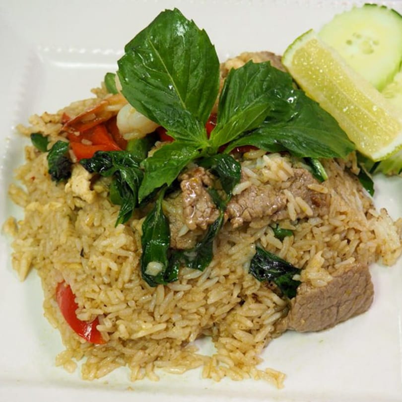 Thai fried rice with beef, basil, red peppers, and a lime wedge on a white plate.