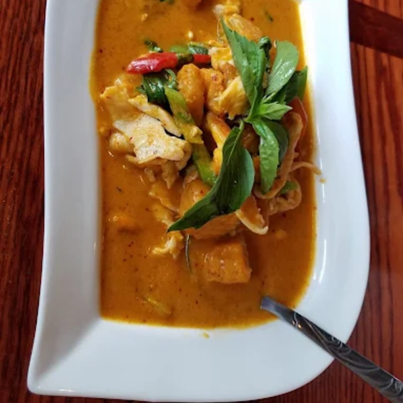 A white rectangular dish filled with orange Thai curry, chicken, basil, and red chili.