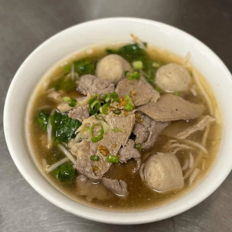 Tong Thai beef noodle soup with sliced beef, meatballs, and green onions in a white bowl.