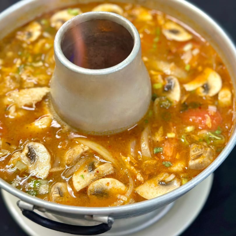 A close-up of a Thai hot pot filled with a rich, spicy broth, mushrooms, and vegetables.