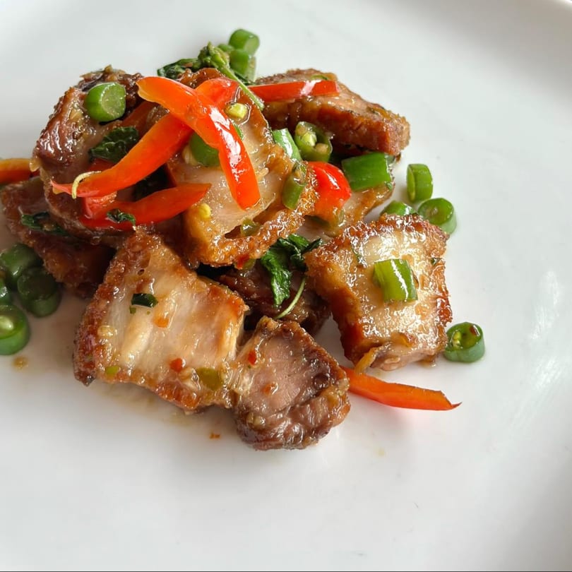 Crispy pork belly stir-fried with red and green chilies and basil on a white plate.