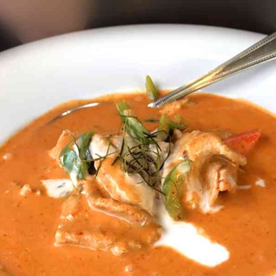 Tong Thai red curry with chicken, green peppers, and herbs in a white bowl with a spoon.