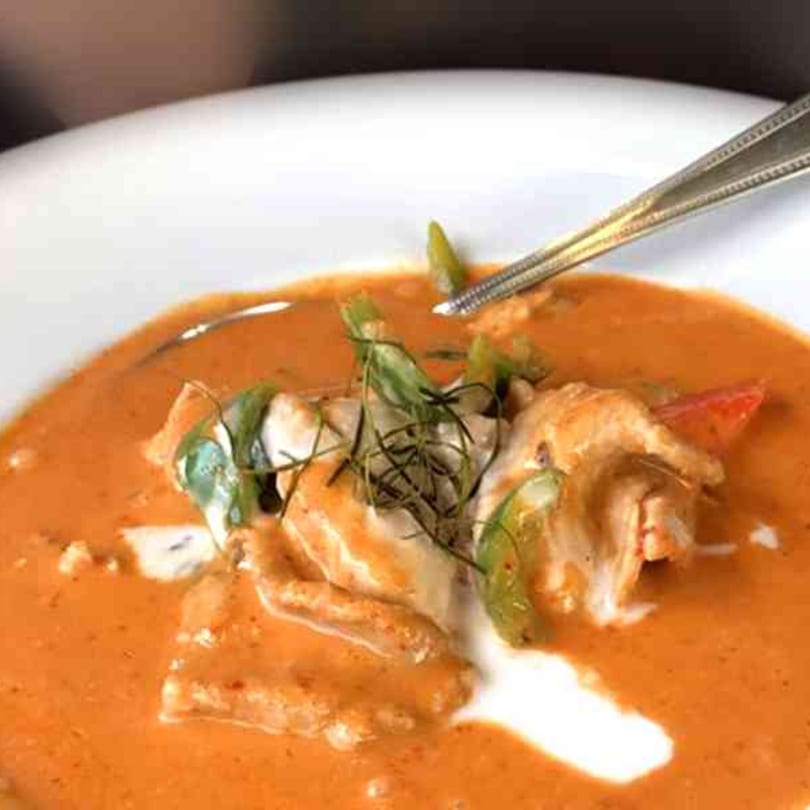 Tong Thai red curry with chicken, green peppers, and herbs in a white bowl with a spoon.
