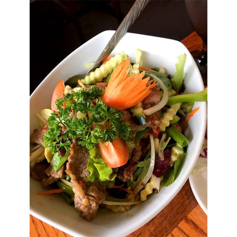 Tong Thai beef salad with fresh vegetables, herbs, and a carved carrot garnish.