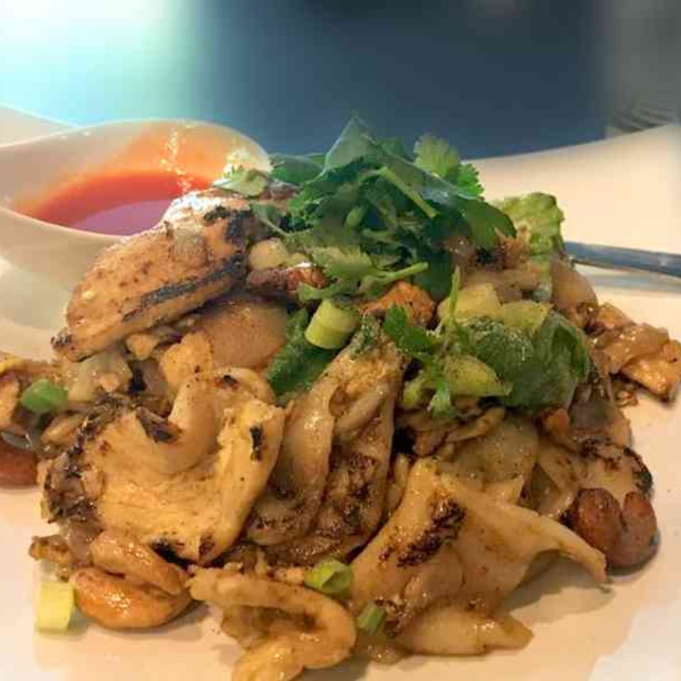 Tong Thai's chicken and noodles with cilantro, green onions, and a side of red sauce.