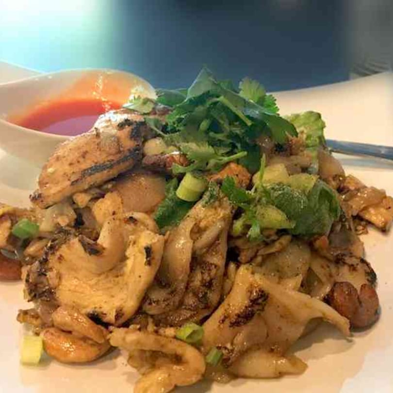 Tong Thai's chicken and noodles with cilantro, green onions, and a side of red sauce.