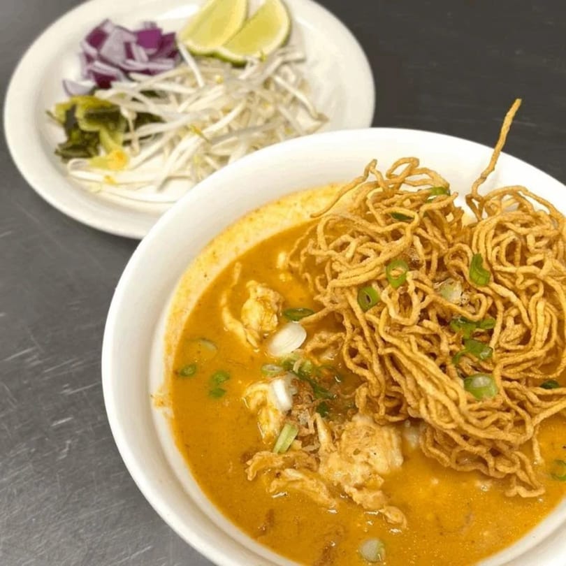 Tong Thai's Khao Soi, a rich curry noodle soup with crispy noodles and a side of fresh garnishes.